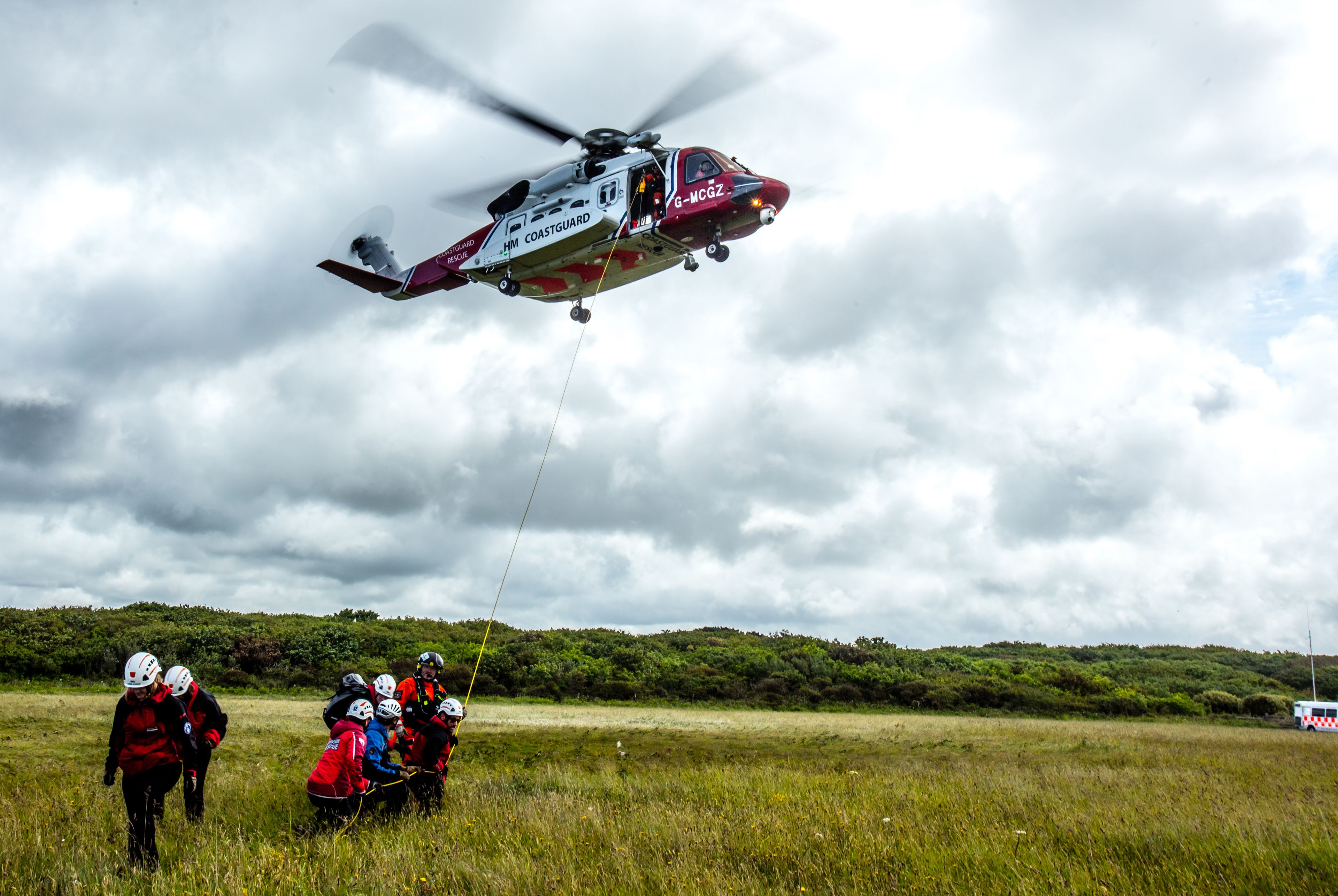 coastguard helicopter flying above moorland with search and rescue team below