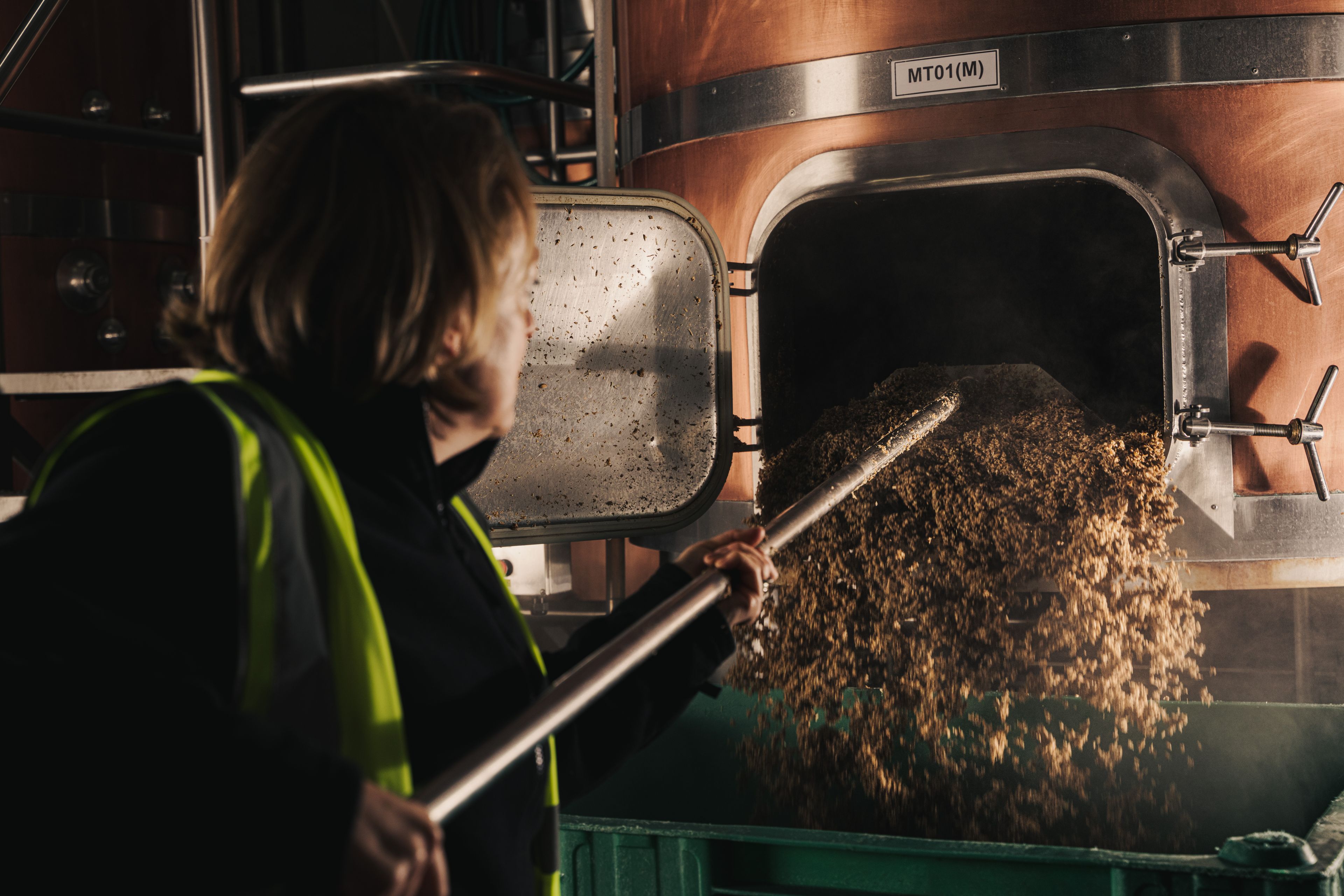 woman using tool to pull spent grain and hops out of a mashtun in brewery